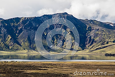 Dramatic iceland landscape with a green hill and black lava and and blue mirror mountain lake. Iceland Stock Photo