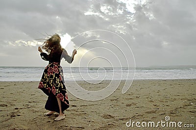 Dramatic portrait of long haired lady in floral formal dress on a stormy beach in front of the sun Stock Photo