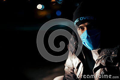 Dramatic portrait of a man in a blue protective mask during quarantine. Night street. Hard light. Coronavirus. Quarantine. Caption Stock Photo