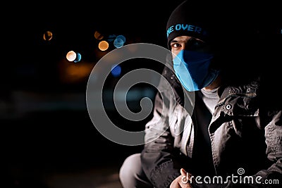 Dramatic portrait of a man in a blue protective mask during quarantine. Night street. Hard light. Coronavirus. Quarantine. Caption Stock Photo