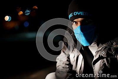 Dramatic portrait of a man in a blue protective mask during quarantine. Night street. Hard light. Coronavirus. Quarantine. Caption Stock Photo