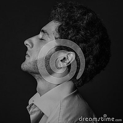 Dramatic portrait of a man theme: man sitting in profile wearing a shirt with closed eyes on a dark background in the studio Stock Photo