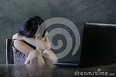 Dramatic portrait of scared and stressed teenager girl or young woman with laptop computer suffering cyber bullying stalked and in Stock Photo