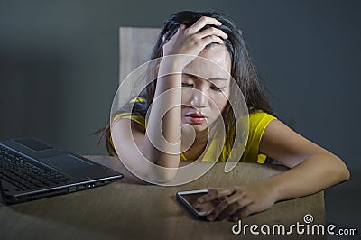 Dramatic portrait scared and stressed Asian Korean teen girl or young woman with laptop computer and mobile phone suffering cyber Stock Photo