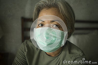 Scared and worried middle aged woman 50s with grey hair and protective mask during covid-19 virus crisis home lockdown quarantine Stock Photo
