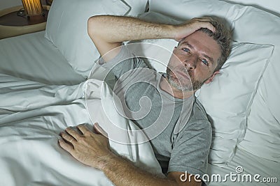 Dramatic portrait of stressed and frustrated man in bed awake at night suffering insomnia sleeping disorder tired and desperate Stock Photo