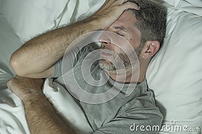 Dramatic portrait of stressed and frustrated man in bed awake at night suffering insomnia sleeping disorder tired and desperate Stock Photo
