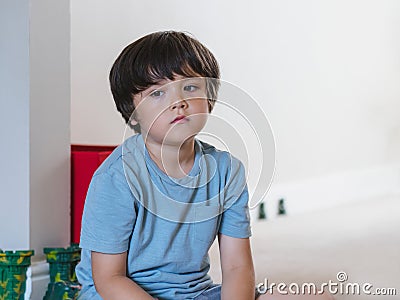 Dramatic portrait tired kid siting alone and lookig out deep in throught, Bored child siting on floor with unhappy face, Lonely Stock Photo