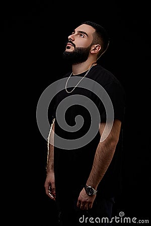 A dramatic portrait of a young serious guy, musician, singer, rapper with a beard in black clothes on a black isolated background Stock Photo