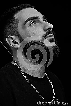 A dramatic portrait of a young serious guy, musician, singer, rapper with a beard in black clothes on a black isolated background Stock Photo