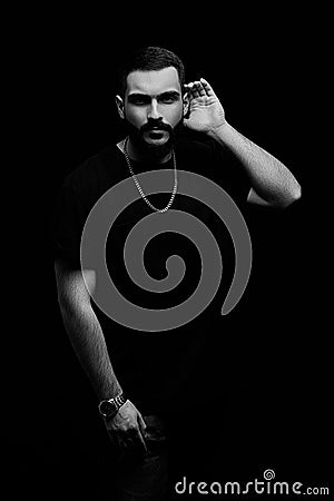 A dramatic portrait of a young serious guy, musician, singer, rapper with a beard in black clothes on a black isolated background Stock Photo