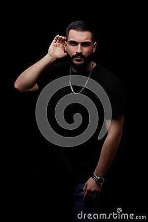 A dramatic portrait of a young serious guy, musician, singer, rapper with a beard in black clothes on a black isolated background Stock Photo