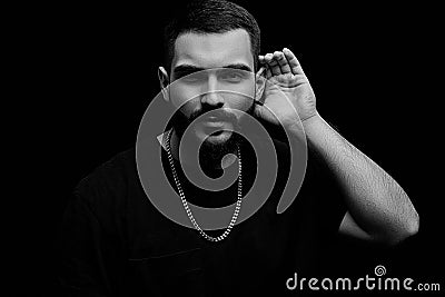 A dramatic portrait of a young serious guy, musician, singer, rapper with a beard in black clothes on a black isolated background Stock Photo