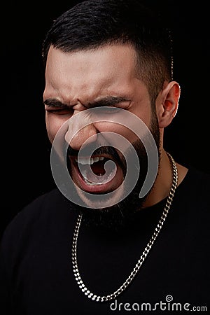 A dramatic portrait of a young serious guy, musician, singer, rapper with a beard in black clothes on a black isolated background Stock Photo