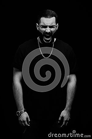 A dramatic portrait of a young serious guy, musician, singer, rapper with a beard in black clothes on a black isolated background Stock Photo