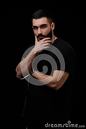 A dramatic portrait of a young serious guy, musician, singer, rapper with a beard in black clothes on a black isolated background Stock Photo