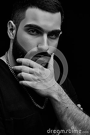 A dramatic portrait of a young serious guy, musician, singer, rapper with a beard in black clothes on a black isolated background Stock Photo