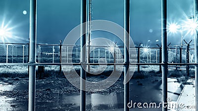 Dramatic Shot Of High Security Prison Facility Yard From Inside Iron Bars During Rain Storm At Night Stock Photo