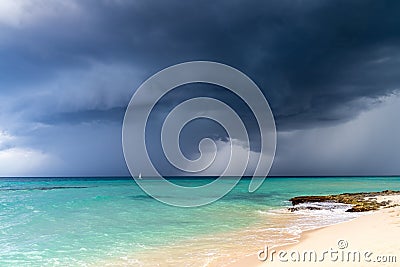 Dramatic view of dark grey storm clouds against the turquoise blue water of the Caribbean sea and a white sand beach Stock Photo