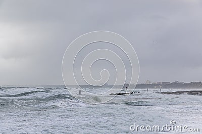 A dramatic view of a very choppy sea with huge crashing waves on groynes breakwater during a major storm under a grey sky Stock Photo