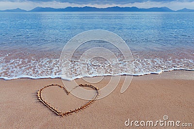 A drawing of a heart as a love symbol on a yellow sand at sea Stock Photo