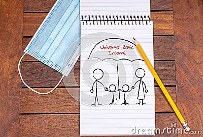 Drawing on note pad of family under the protective umbrella of universal basic income, next to face mask Stock Photo