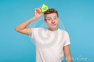 Dreaming of home purchase. Positive thoughtful man in t-shirt holding small paper house on head Stock Photo