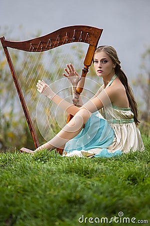 Dreaming sensual female harpist in light dress playing music in park outdoor Stock Photo