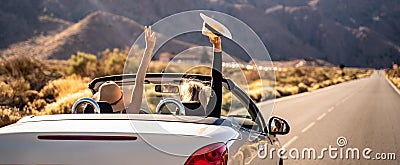 Dreams come true! Two happy young girls driving cabrio car during vacation road trip in mountains, making memories and having fun Stock Photo