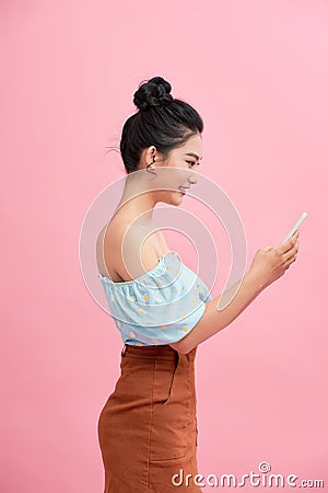 Dreamy asian beauiful young woman holds modern electronic device, isolated over pink background Stock Photo