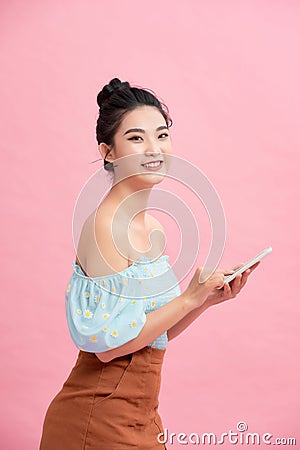 Dreamy asian beauiful young woman holds modern electronic device, isolated over pink background Stock Photo