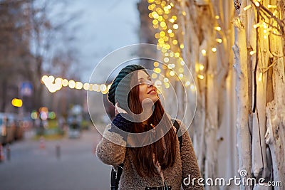 Dreamy caucasian woman walking in the street. City lights. Winter casual clothes. Festive city at the evening. Copy Stock Photo