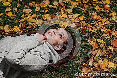 Fall portrait of a girl lying on a lawn in a forest park. Long hair on yellow foliage. Stock Photo