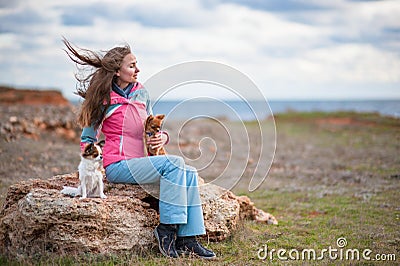 Dreamy girl sitting with two little dogs on cold sea shore with copy space Stock Photo