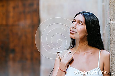 Dreamy Hispanic traveler leaning on wall Stock Photo