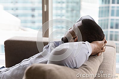 Dreamy sleepy young Black man relaxing on couch Stock Photo