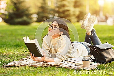 Dreamy student girl reading book, resting in park Stock Photo