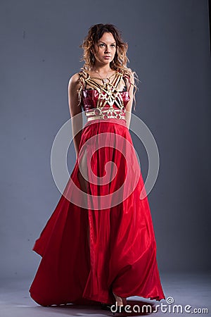 Girl in a red long dress in the studio, on a gray background. Stock Photo