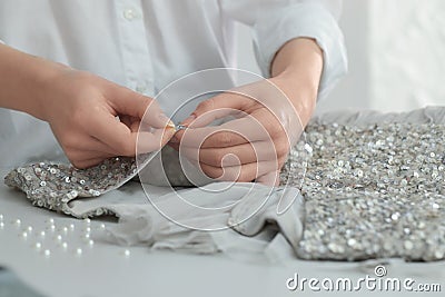 Dressmaker sewing party dress from silver fabric with paillettes at table in atelier, closeup Stock Photo