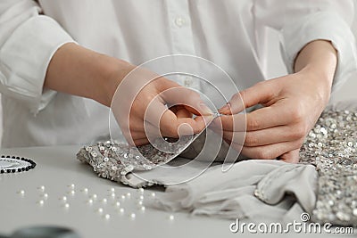 Dressmaker sewing party dress from silver fabric with paillettes at table in atelier, closeup Stock Photo