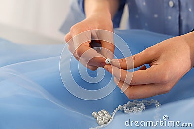 Dressmaker stringing bead on thread at light blue fabric in atelier, closeup Stock Photo