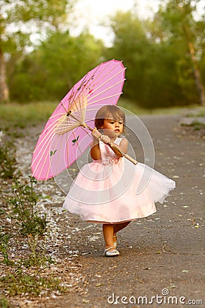 Dressy two-year-old girl carrying pink parasol Stock Photo