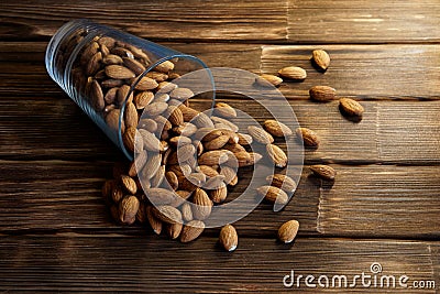 Dried almond nuts in tilted transparent blue glass on a wooden background Stock Photo