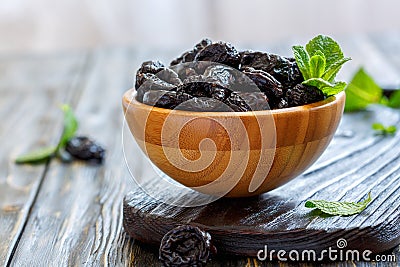 Dried black plums and mint in a wooden bowl. Stock Photo