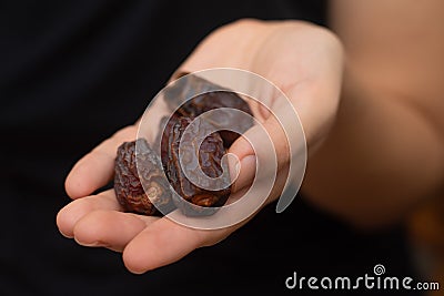 Dried Dates in Female Hand. Offering a handful of glossy, sweet dried dates Stock Photo