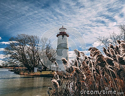 Dried grass near the lake with a white lighthouse in the background under the cloudy sky Stock Photo