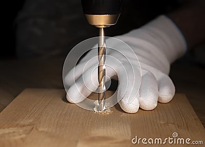 Drilling working process closeup. Modern steel drill tool making hole in wood and hands in builder gloves Stock Photo