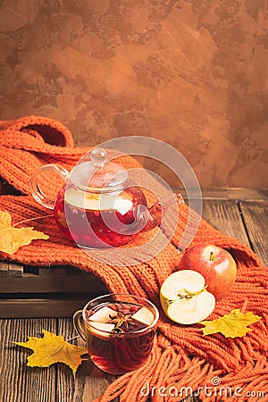 Drink autumn apple red berries in a glass teapot and an orange scarf on a wooden background. Hot fruit berry tea. Stock Photo