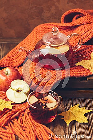 Drink autumn apple red berries in a glass teapot and an orange scarf on a wooden background. Hot fruit berry tea. Stock Photo