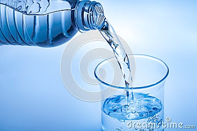 Drink water pouring in to glass over light blue background Stock Photo